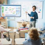 An engaging teacher explains complex concepts to attentive students in a modern classroom setting, utilizing digital tools and whiteboards for interactive learning.